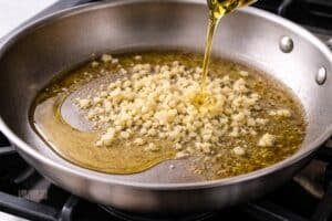 Finely chopped garlic cooking in olive oil in a skillet, lightly sizzling without browning on a clean stovetop